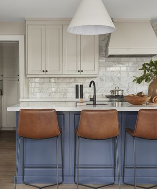 A backsplash idea for kitchens with marble subway tiles, blue island and leather bar chairs