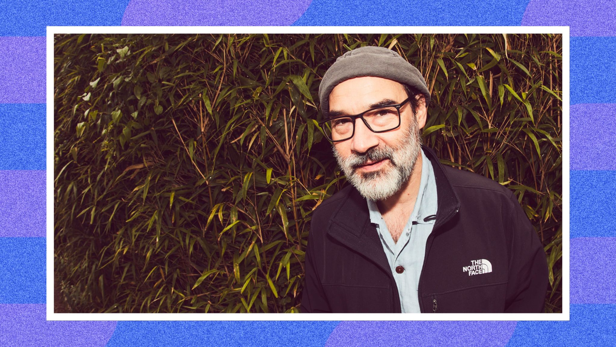 A photo of Adam Buxton in front of some leafy bushes.