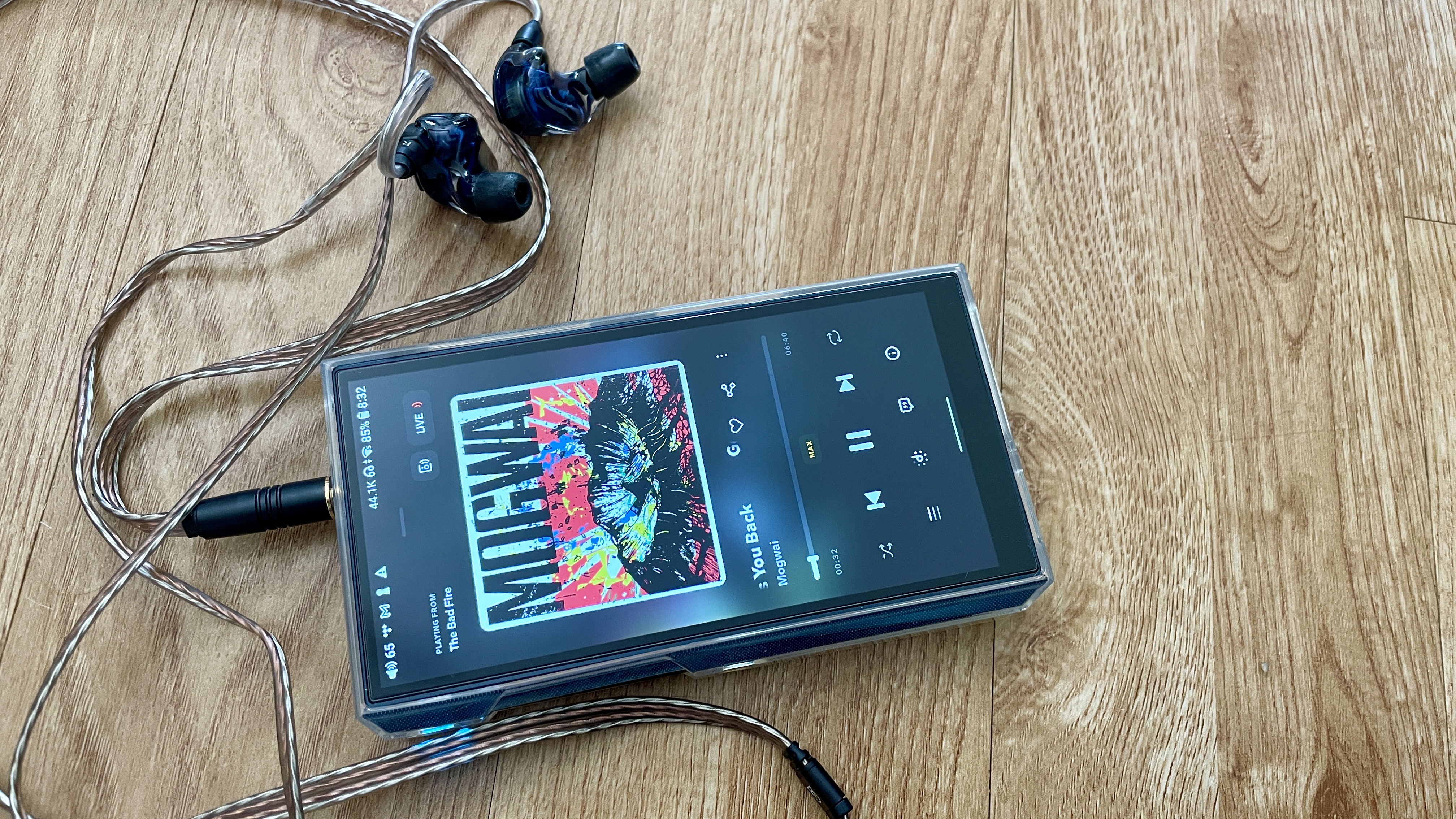 FiiO M23 player in a woman's hand, above a wooden table, playing Mogwai, Gunna and Fontaines DC