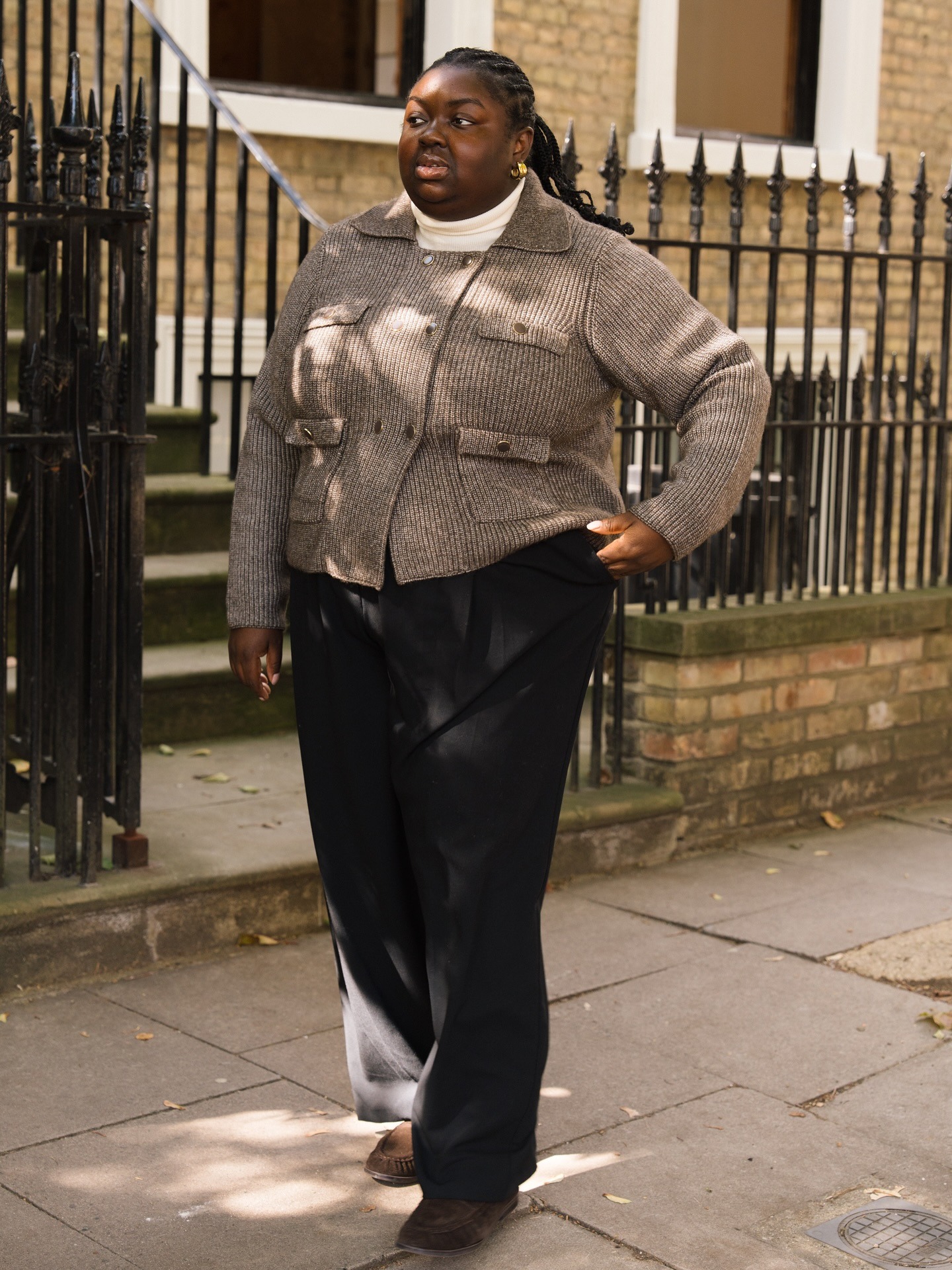 Abi wears a brown cardigan, black pants, and suede loafers.
