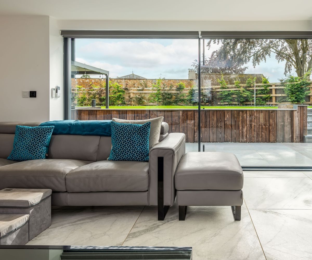 Minimalist living room with large-format stone tiles and grey sofa in front of Kloeber slimline sliding doors