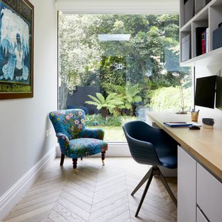 Study area with parquet floor, desk and blue armchair in front of large picture window to garden