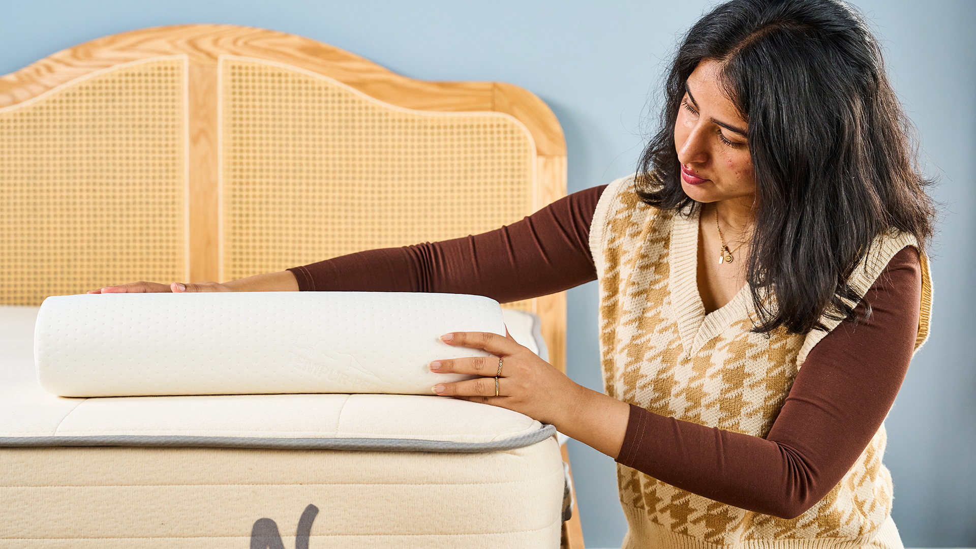 Woman placing her hand over a curved white bedroom against the backdrop of a wooden rattan headboard of the bed