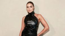 Olivia Culpo wearing a black halterneck leather dress with brown tied back hair in front of a beige background