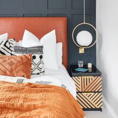 bedroom with large bed, rust and white bedding, bedside table and navy wall panelling