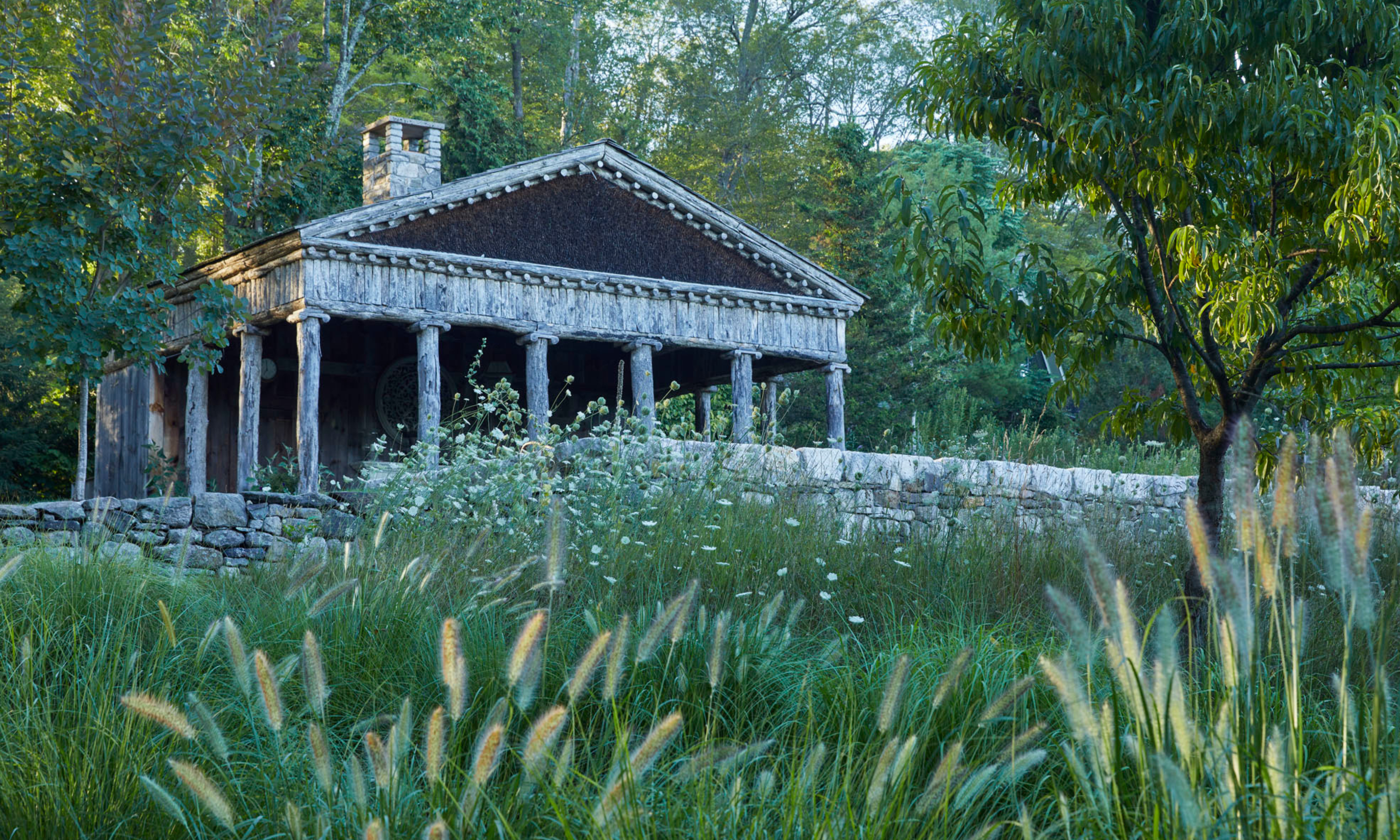 Greek-style building with pillars in garden surrounded by mature trees