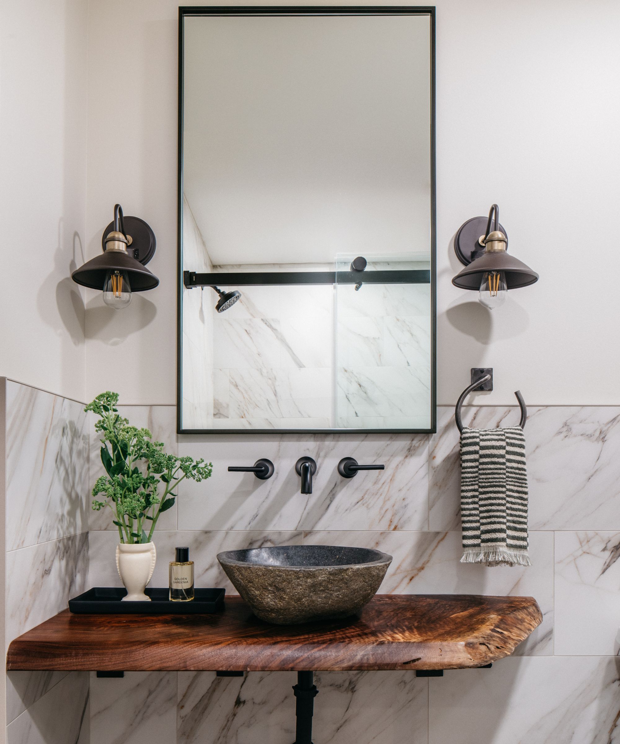 A guest bathroom with white walls, marble tiles, and a wooden vanity topped with a stone sink