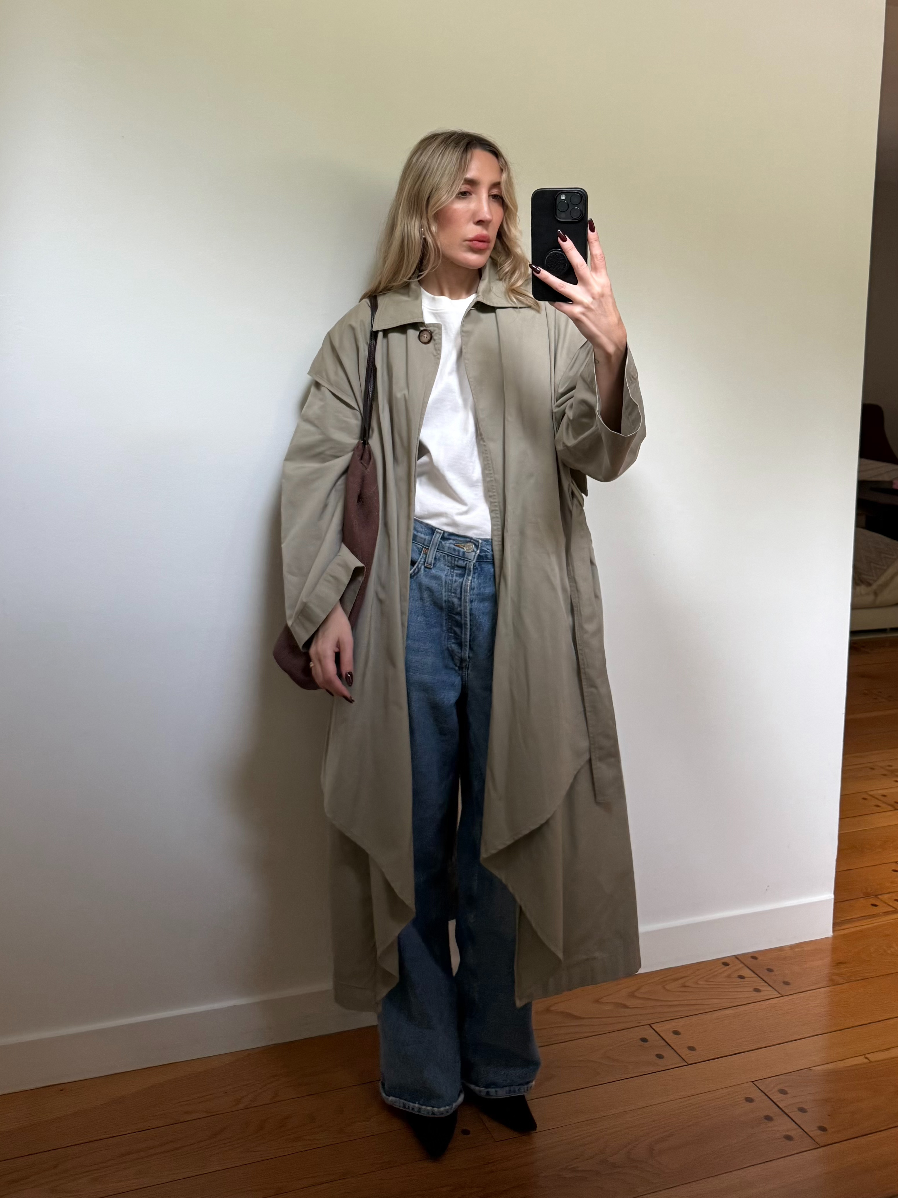 Angela Fink wearing a trench coat, a T-shirt, jeans, and boots