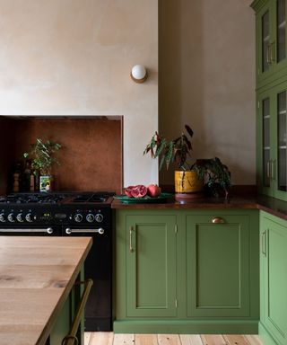 corner of kitchen with olive green cabinets, plaster walls and black cooker