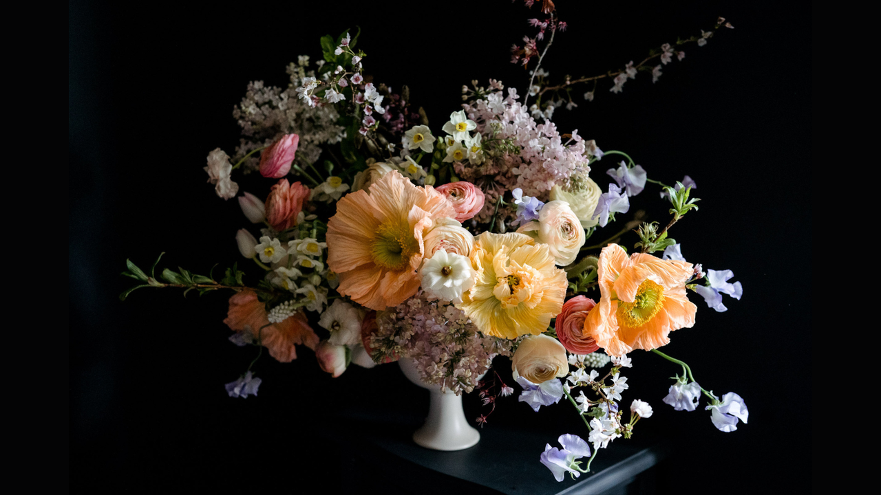 A large pastel-coloured floral design in cream footed bowl on black background