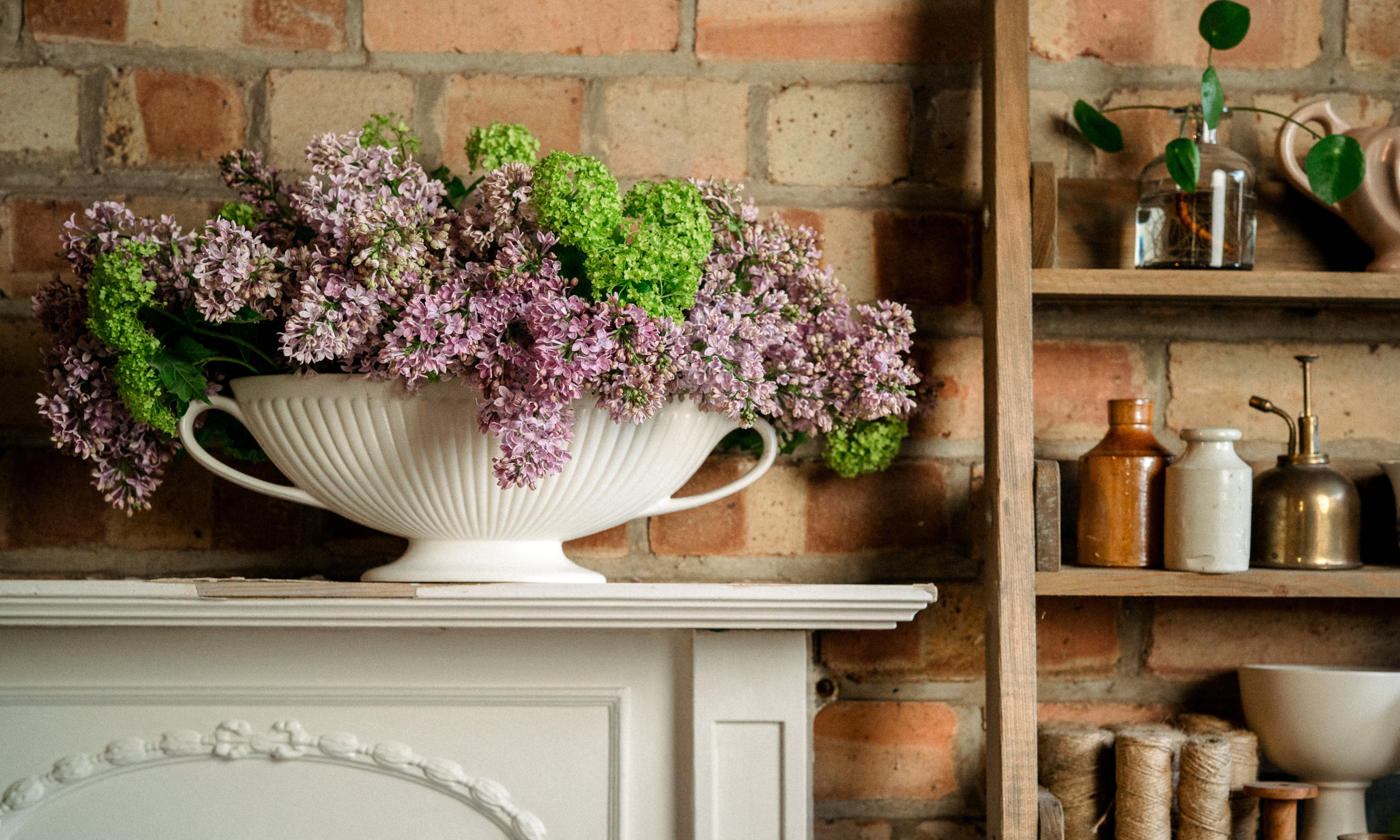 Floral design with abundance of lilac and green viburnum opulus roseum on mantlepiece in front of brick wall