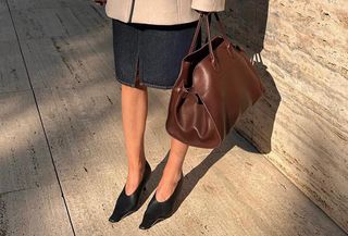 @iliridakrasniqi wearing a skirt, pumps, a blazer, and a brown The Row Margaux bag.