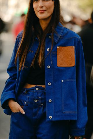 A woman at Paris Fashion Week wearing a blue Loewe denim jacket, black top, and blue jeans.