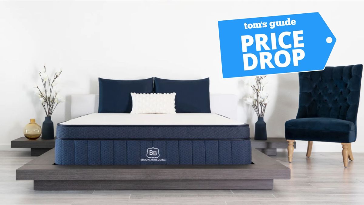 Brooklyn Bedding Aurora Luxe navy and white cooling mattress on wooden bed base in bedroom with grey wooden floor and Tom&#039;s Guide price drop badge