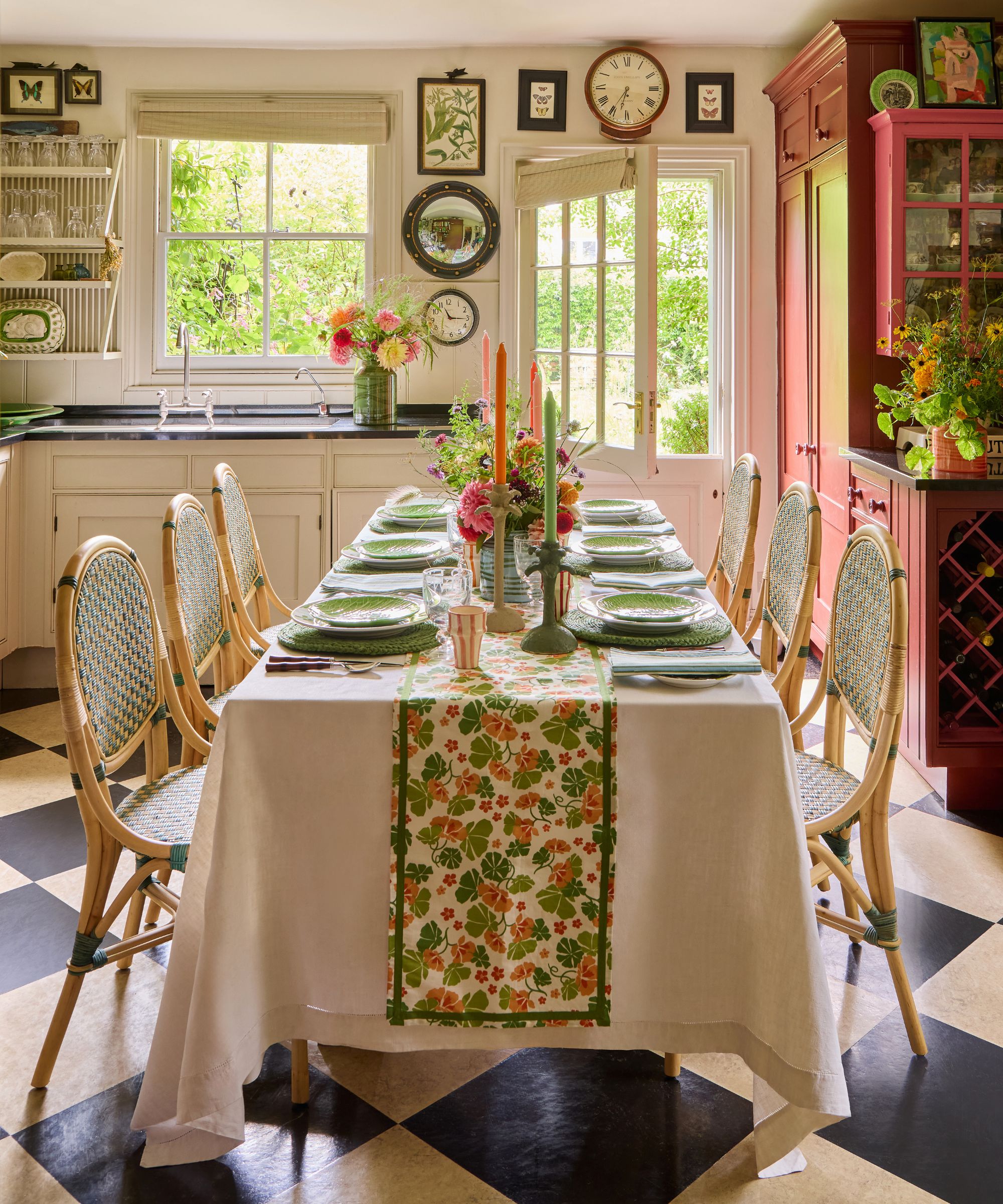 country kitchen with neutral cabinets, black and white kitchen floor, with a red pantry cupboard and a long table styled for a summer dinner party