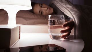 Woman reaching out to a glass of water kept on the bedside table at night