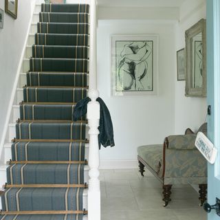 Open light blue door with sign of "Gone to the beach" hanging on it in front of white stair case with shades of green stair case runner