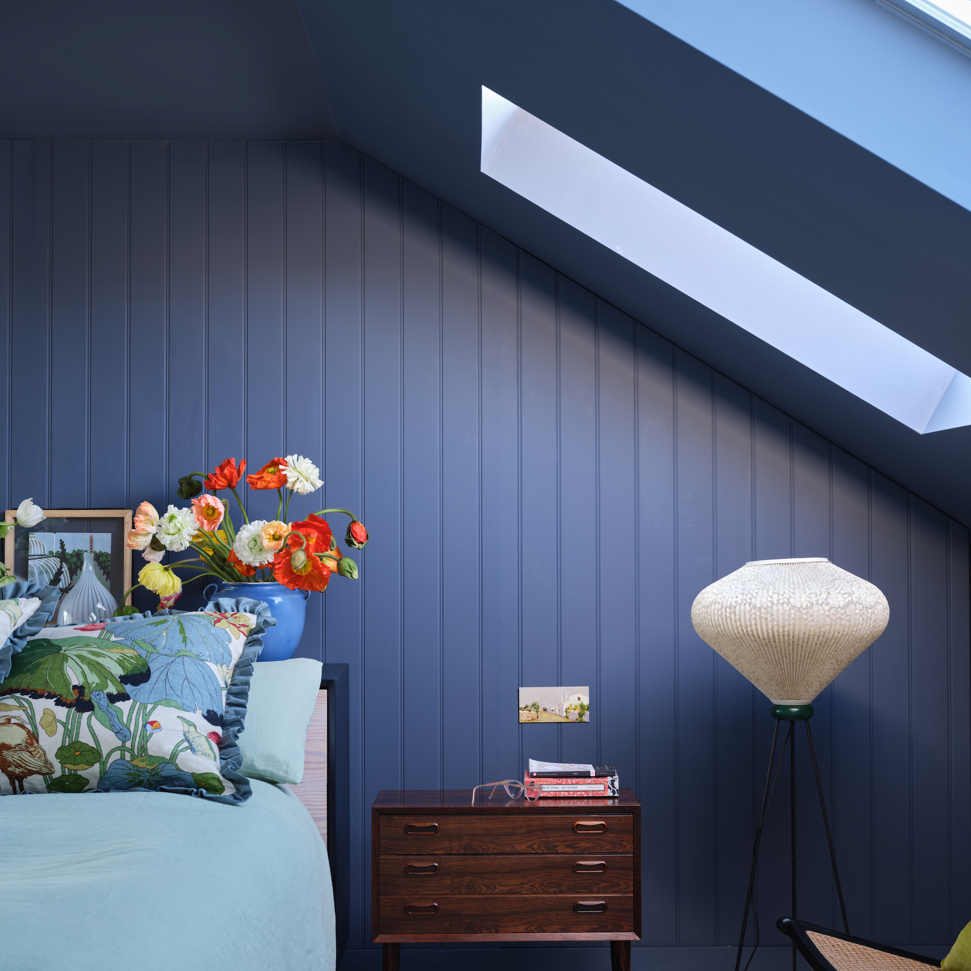 loft bedroom drenched in blue paint with flowers in a vase and floor lamp with white shade