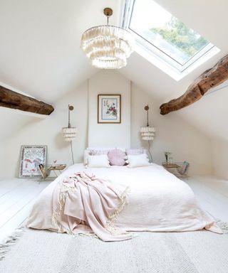 A white bedroom in an attic with two wooden beams down.