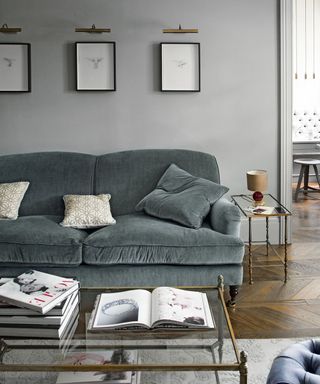 grey living room with wall-mounted picture frames and a grey sofa with patterned cushions and a glass-top coffee table topped with books