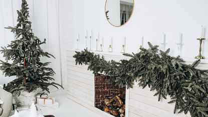 A Christmas garland on a fireplace beside a Christmas tree