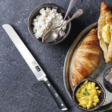 A bread knife is on a counter surrounded by food. 