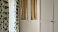 neutral wardrobes with glass front closet door with a cabinet curtain behind and brass hardware