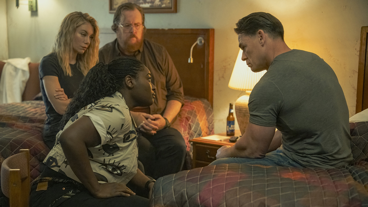 Leota, Harcourt, and Economos sitting as they chat to a seated Chris Smith in a hotel room in Peacemaker season 2 episode 8