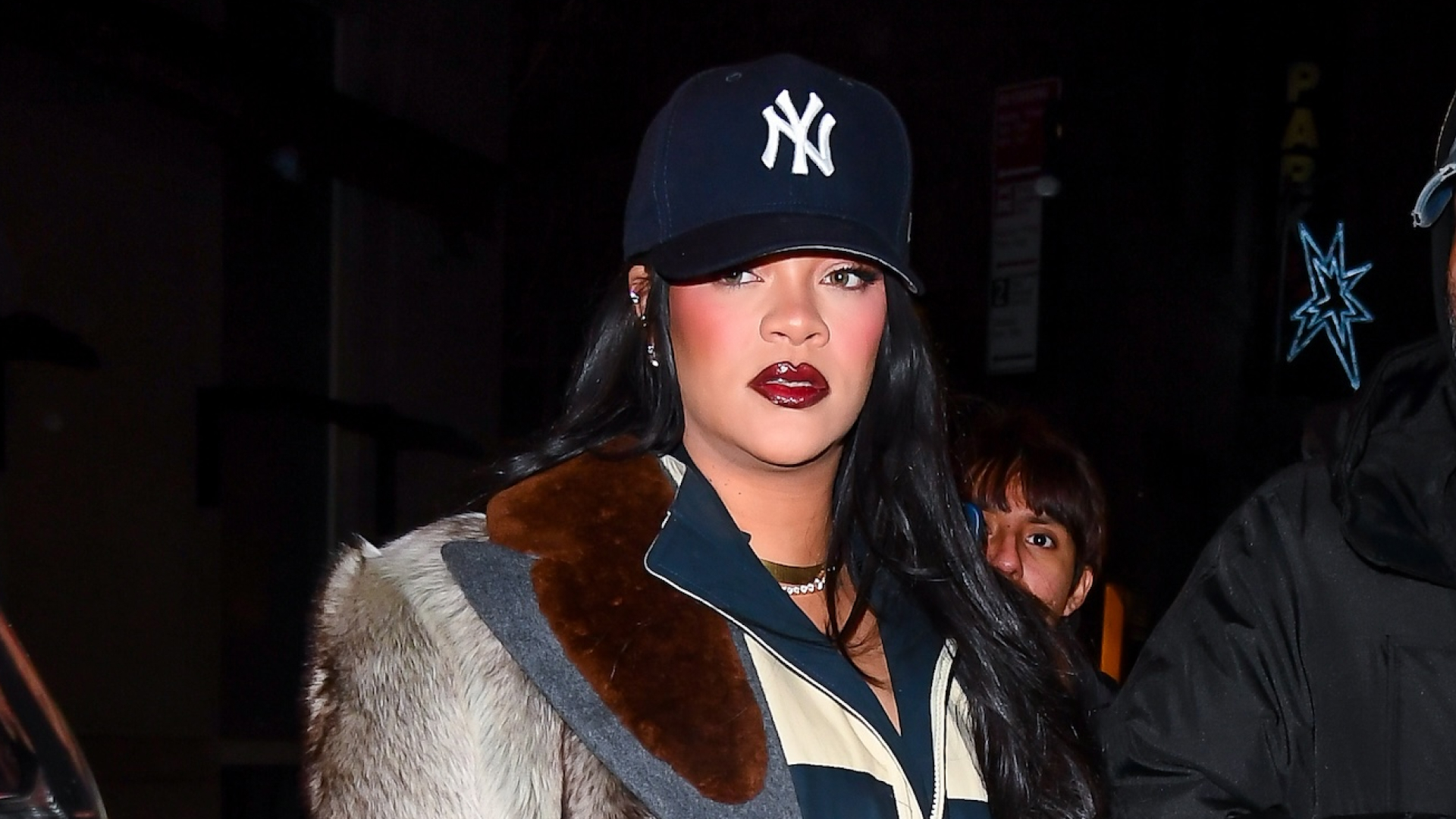 Rihanna in Manhattan on January 17, 2026 wearing a Prada fur coat, Loewe two tone boots, a black skirt, a casual track jacket, and a baseball cap
