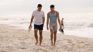 From left to right: Conrad Ricamora and Joel Kim Booster walking down the beach together.