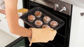 Someone removing muffins from an oven while wearing oven mitts