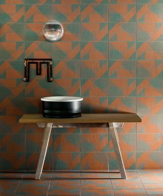 Terracotta and green tiles behind a wooden vanity unit show the warm earth bathroom trend.