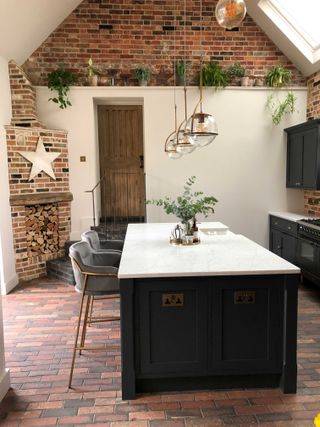 rustic kitchen with exposed brick and white painted walls, terracotta floor tiles and modern kitchen island in the center
