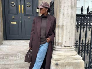 Fashion influencer @nlmarilyn in London wearing a chic winter look with a brown sweater, brown coat, and blue denim jeans, with brown accessories including a cap, suede loafers, and suede bowling bag.