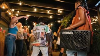Woman carrying Soundboks Go Bluetooth speaker at party.