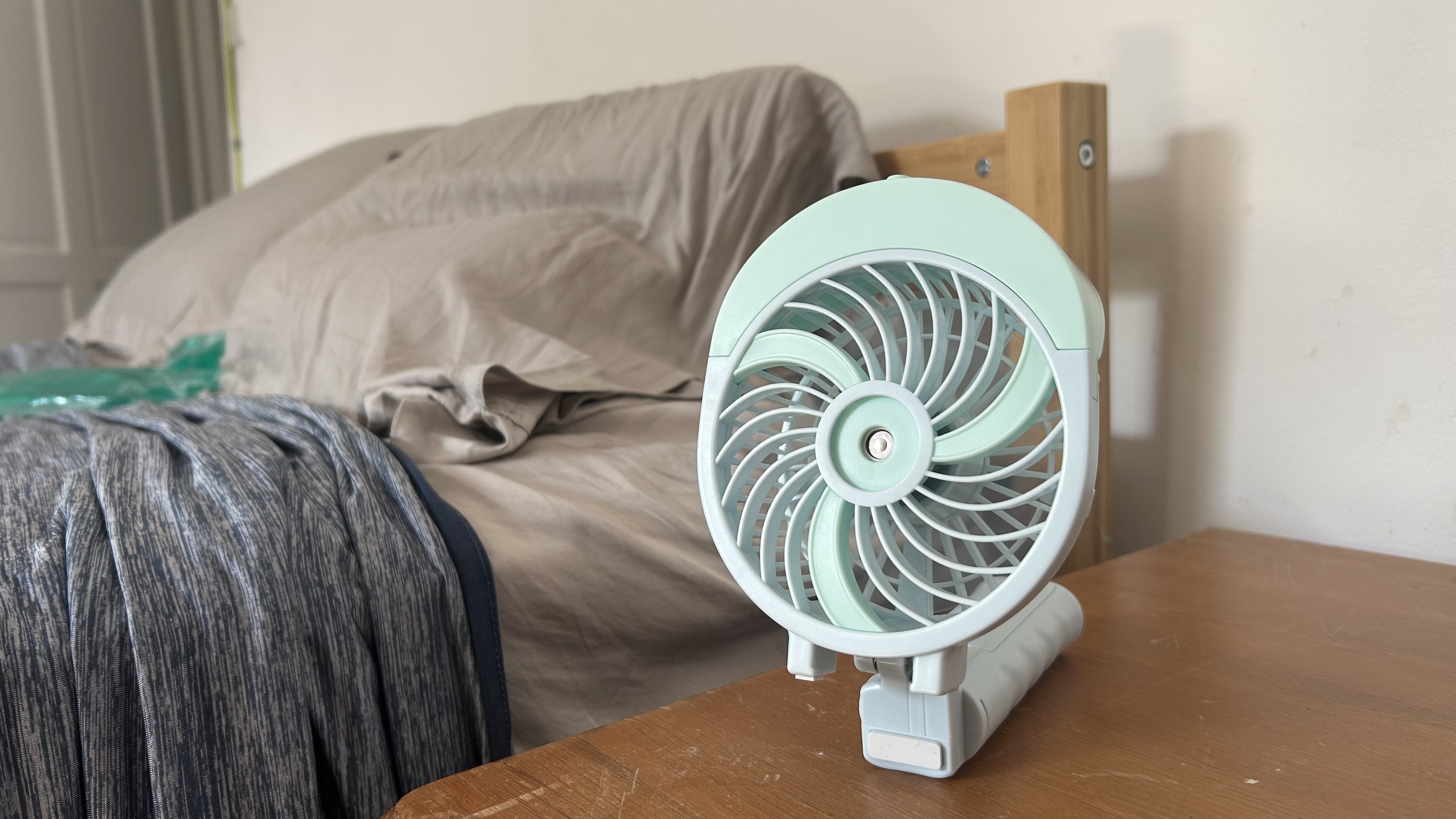 The HandFan Misting Fan balanced on a bedside table with a bed in the background