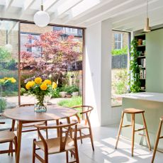 bespoke cladding green kitchen diner with scandi table and chairs large open patio doors and yellow flowers in a vase