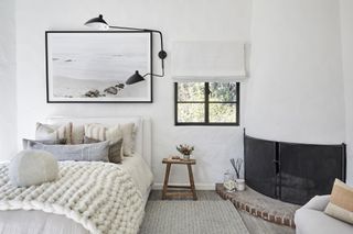 bedroom with double bed, chunky knit bed throw and fireplace in the corner with brick hearth White walls and seascape print on the walls