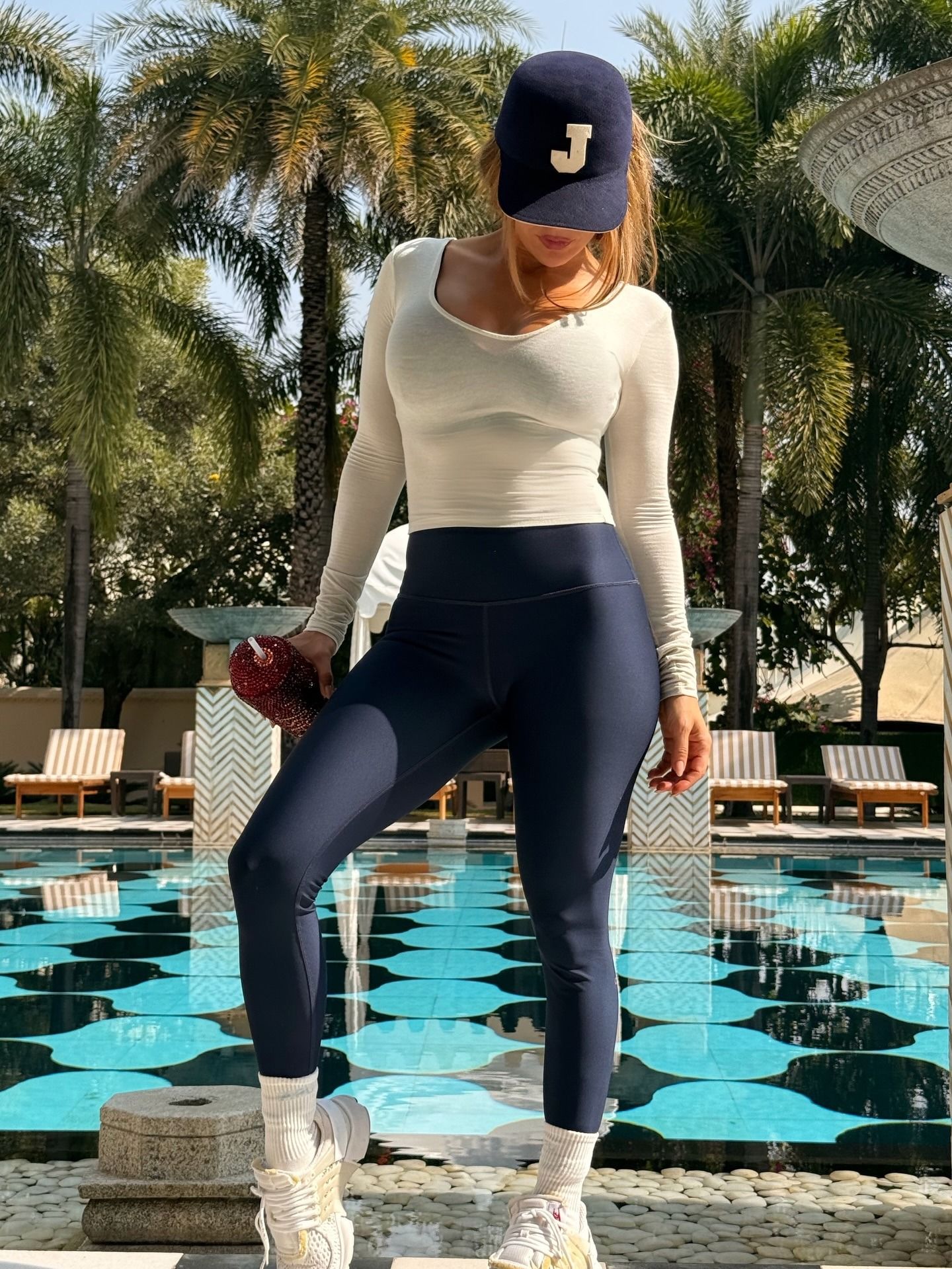 J.lo wears a blue hat with a "J" on it, white long sleeve shirt, navy blue leggings and white sneakers.