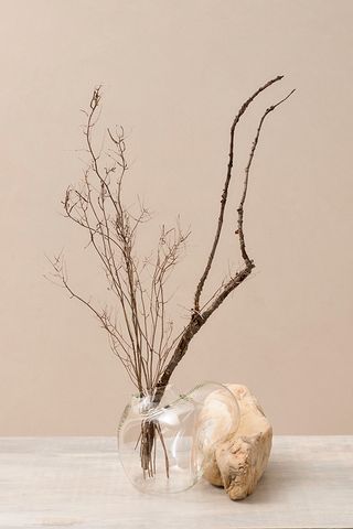 A glass vase that's blown around the rock in light sand color. There are tree branches in the vase.