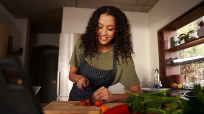 Woman in a kitchen chopping vegetables on a wooden chopping board