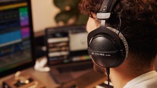 A person wears the Beyerdynamic DT 770 Pro headphones with a computer and keyboard in the background