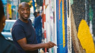 Clive Myrie painting a mural.