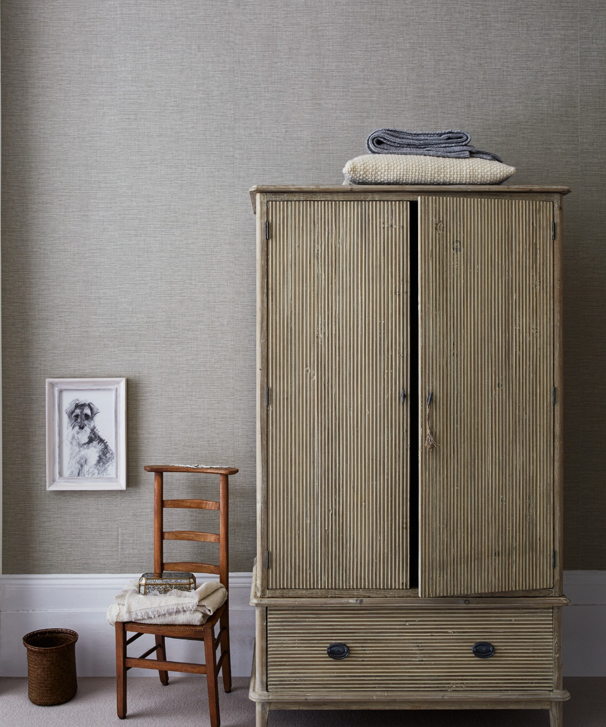 A bedroom with a wardrobe and a chair set against textured, fabric-style wallpaper