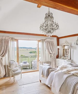 A farmhouse style bedroom with large candle-style chandelier and exposed beams