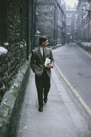 Prince Charles wearing a tweed suit walking down a street in Cambridge, England in 1969 on a cloudy day