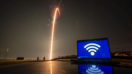 A computer with a large wifi logo sits atop a reflective surface. To the left, in the distance, a streak of light arches into the sky.