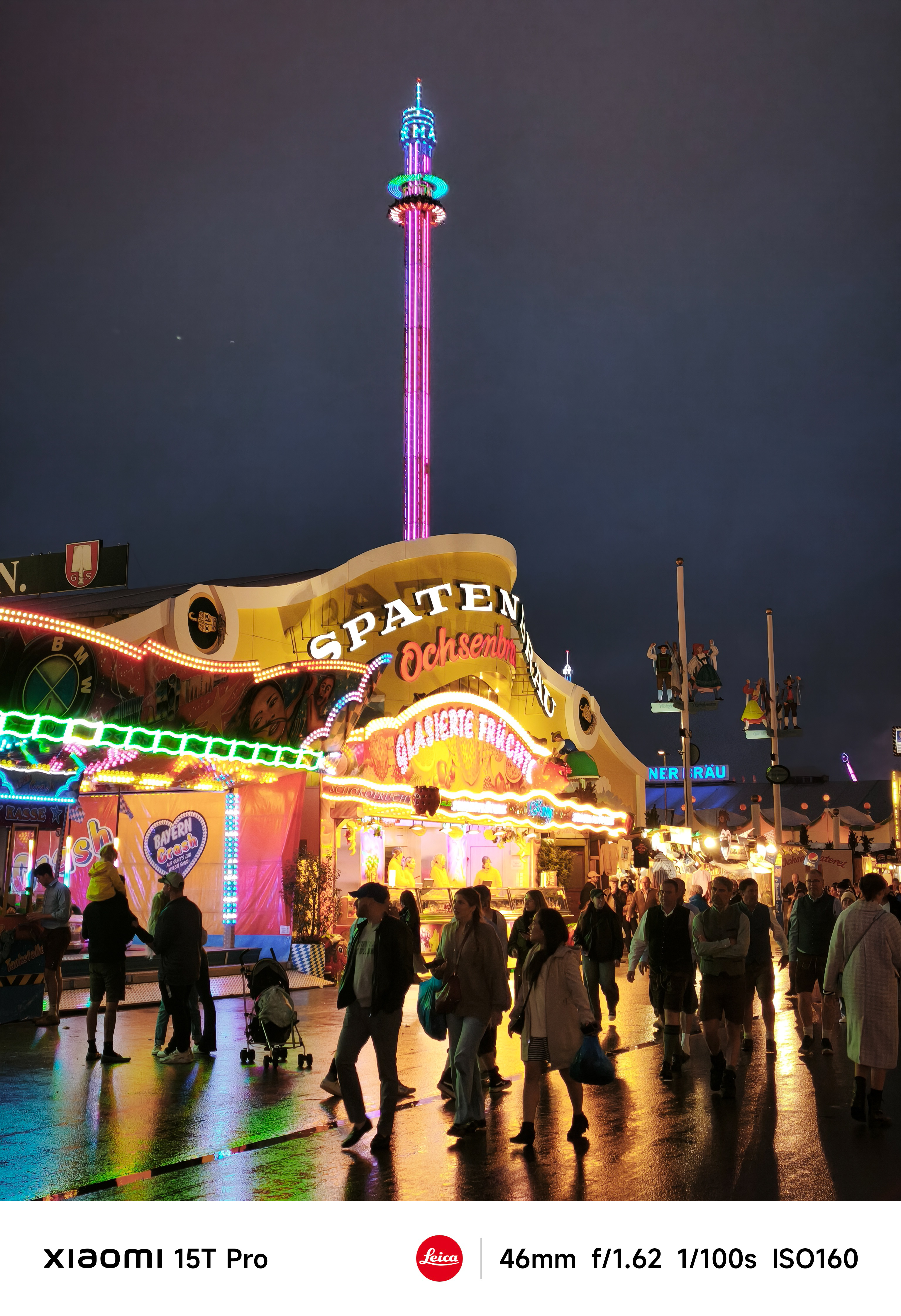 A funfair lit up  colourfully at night with crowds