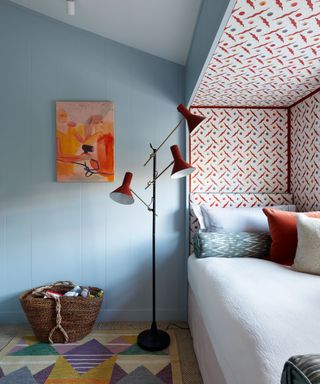Kids room painted in pale blue with red patterned wallpaper around an alcove bed