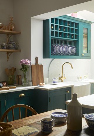 kitchen with teal cabinetry, white countertops, kitchen table, island, wooden shelving, gold tap